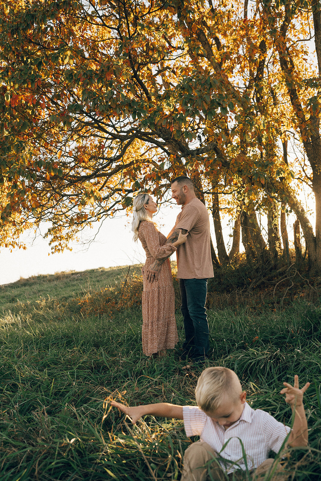 Parents standing in a fall field while their toddler son plays in the foreground during a candid family shoot