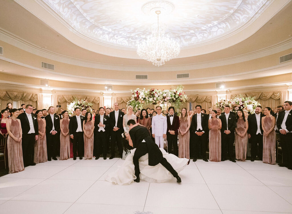 First Dance dip on white dance floor with monogram and wedding party in pink dresses