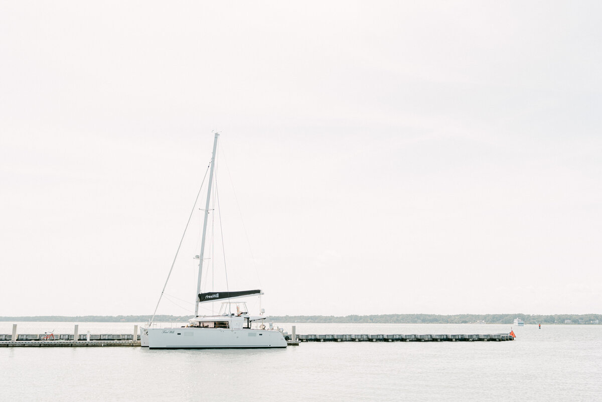 A serene and elegant shot of the "Free Will" yacht docked at Sea Pines Resort. The backdrop features a calm, wide-open sky and tranquil water, embodying the peaceful, romantic atmosphere of the resort. The image highlights the exclusivity of the wedding location, perfect for luxury couples looking for a unique waterfront experience. The photo captures the beauty of the venue, known for hosting intimate and sophisticated weddings. The "As Seen In" section at the bottom references prominent wedding publications that have featured this stunning location.