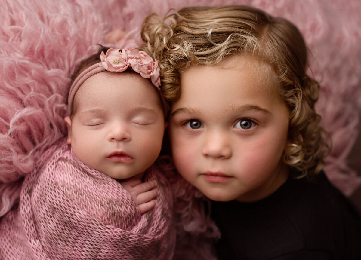 older brother with his baby sister posed on a pink flokati