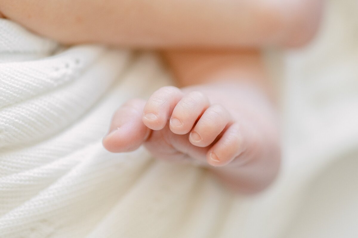 Close up photograph of newborn baby toes against a cream blanket