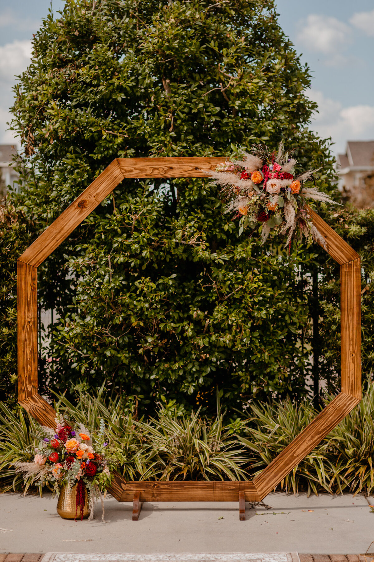 alt="flowers on wooden arch outside wedding"