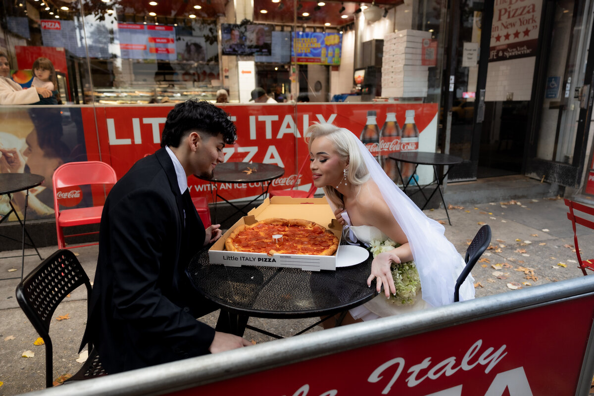 A romantic photo of the couple sharing a pizza under the warm lights of a NYC pizza shop.