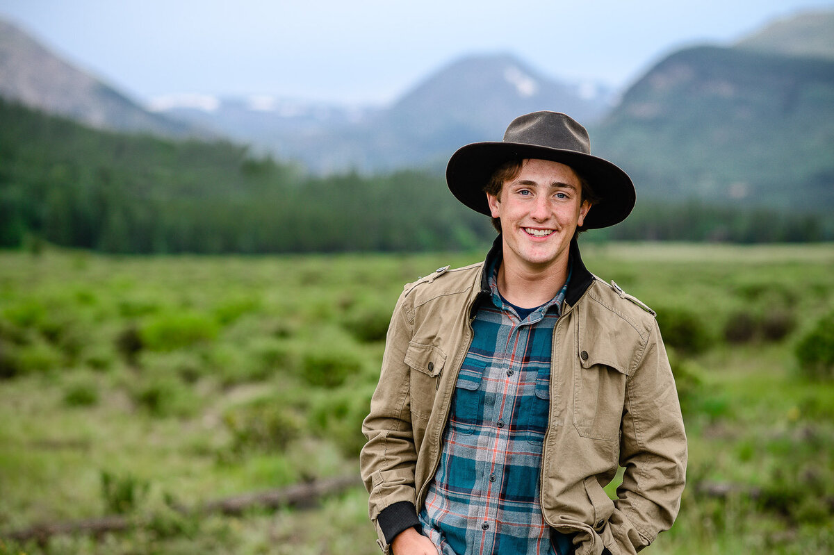 denver senior photographer  photographs senior guy photo ideas with young man in a hat and flannel in the mountains with the woods in the near distance