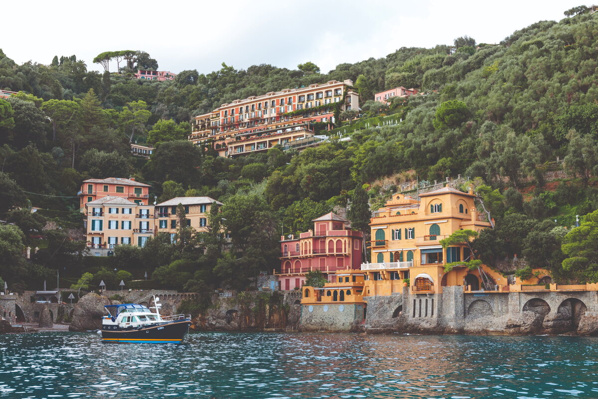 A picturesque view of colorful hillside villas and luxury hotels nestled among lush greenery in Portofino, Italy. The vibrant facades, terracotta rooftops, and Mediterranean charm capture the essence of this iconic Italian Riviera destination.