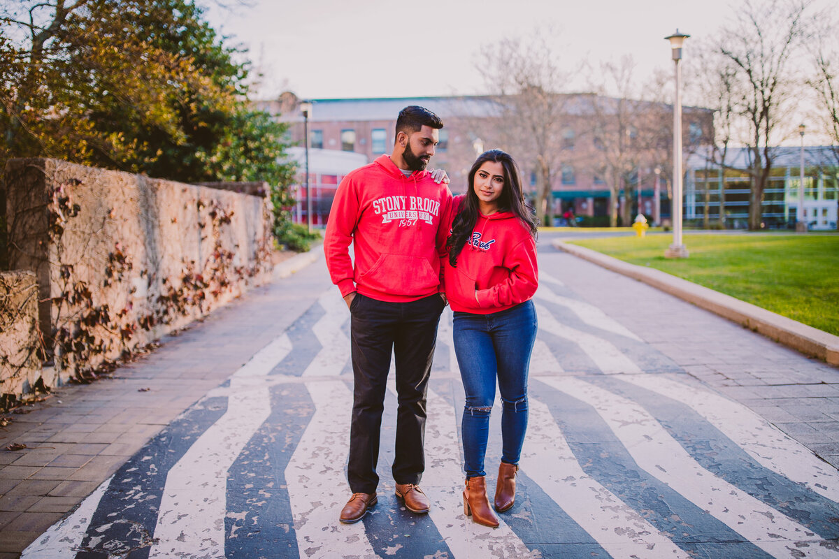 A couple standing on the zebra path at stony brook university during their engagement session at their alma mater in university sweaters