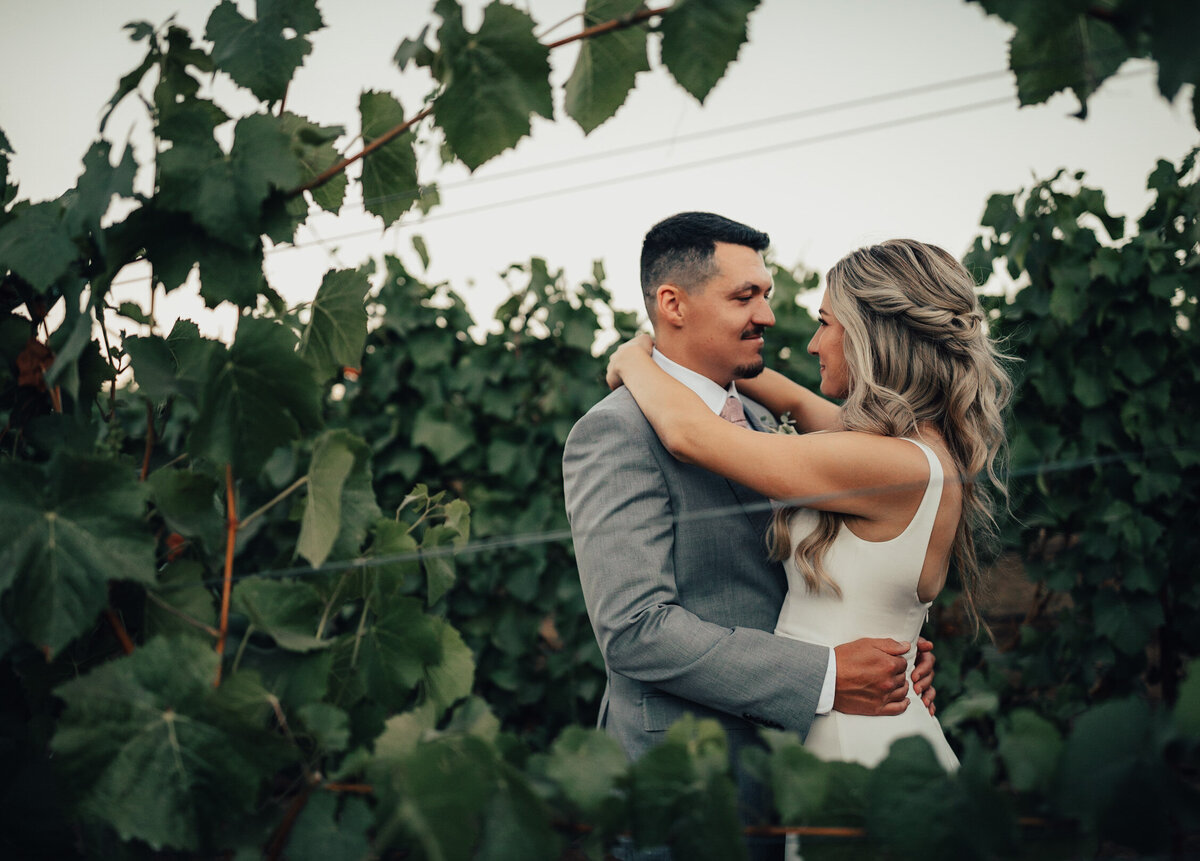 Couple poses together in wine grapes at a vineyard