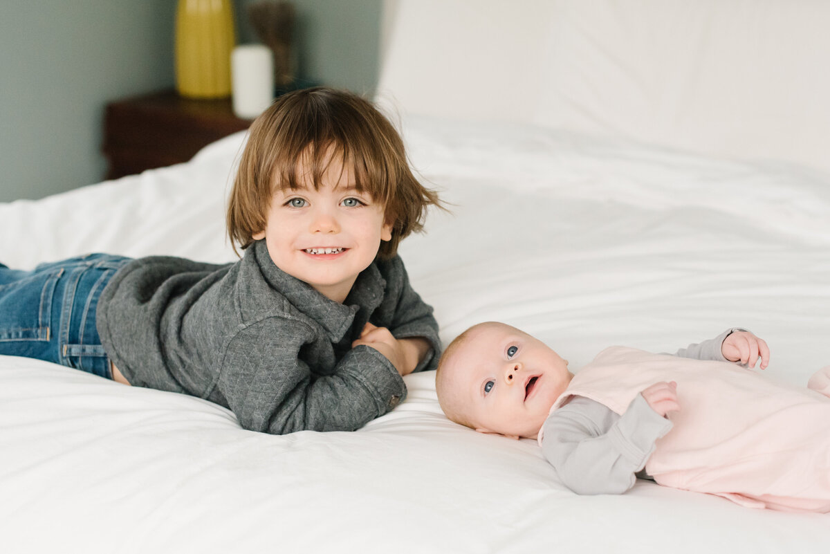 Big brother smiling with baby sibling on cozy bed