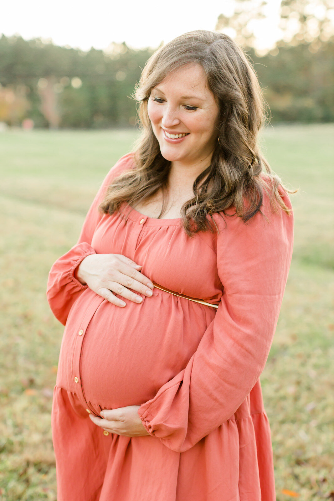 Mom cradles baby bump and smiles down at bump during maternity photo session