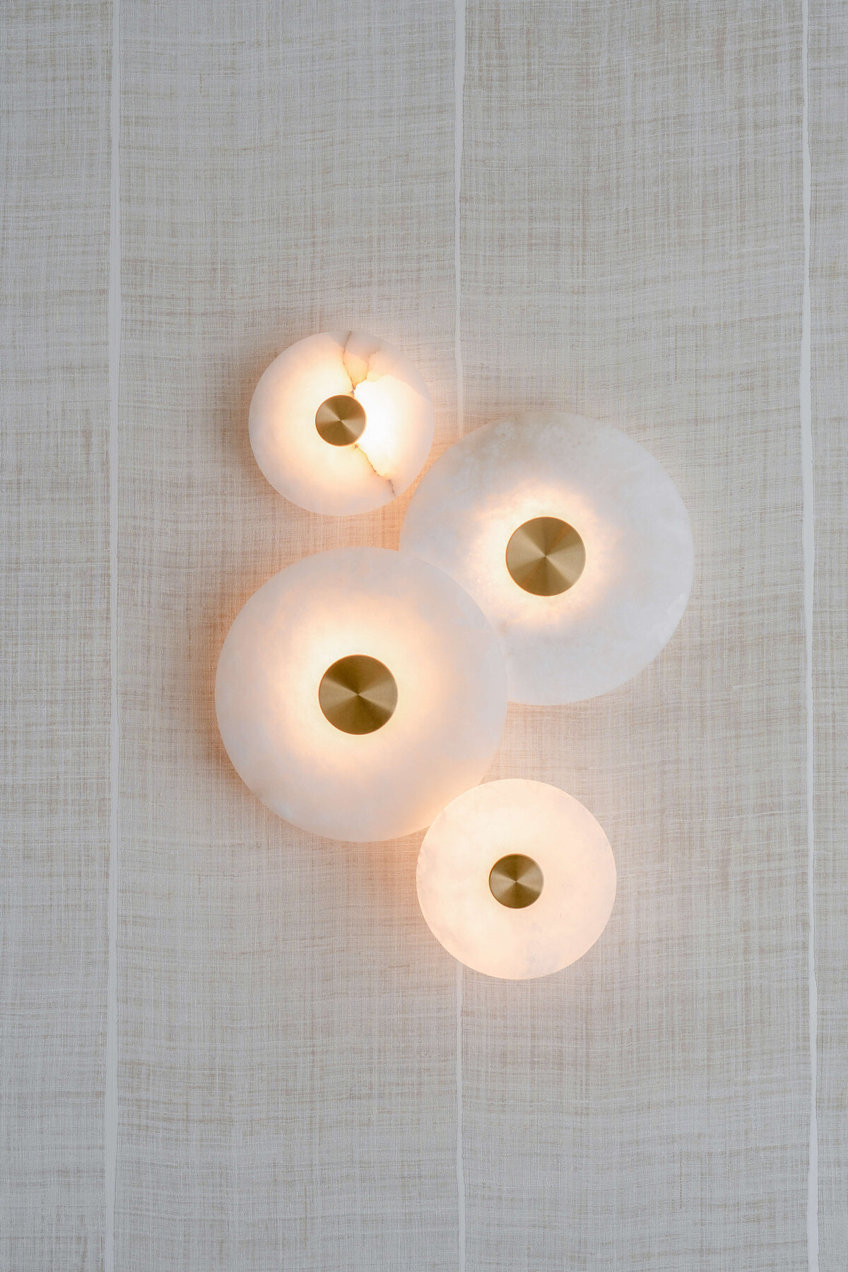 A contemporary wall art piece featuring marble circles of various sizes with gold centers.  The piece is lit and emits a soft, warm light.