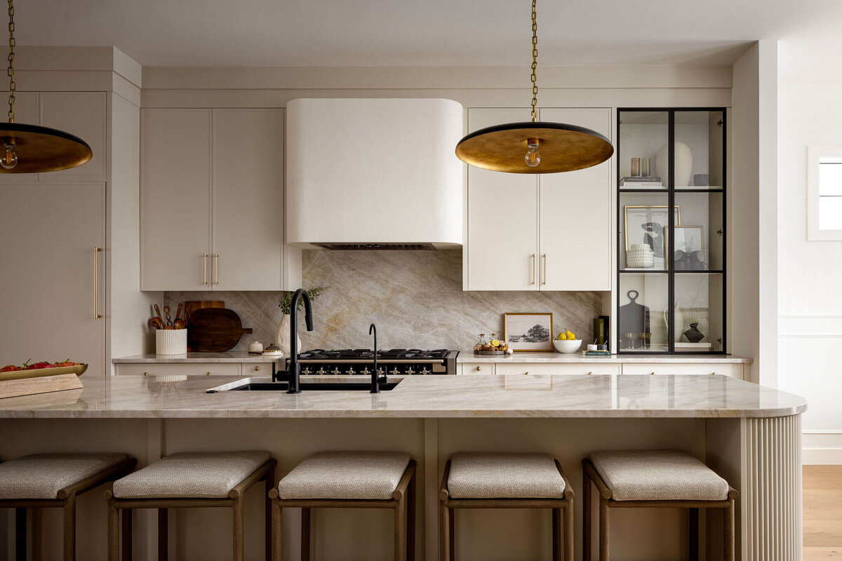 Oval kitchen island with fluted details, plaster hood fan and natural cream cabinets paired with gold hardware.