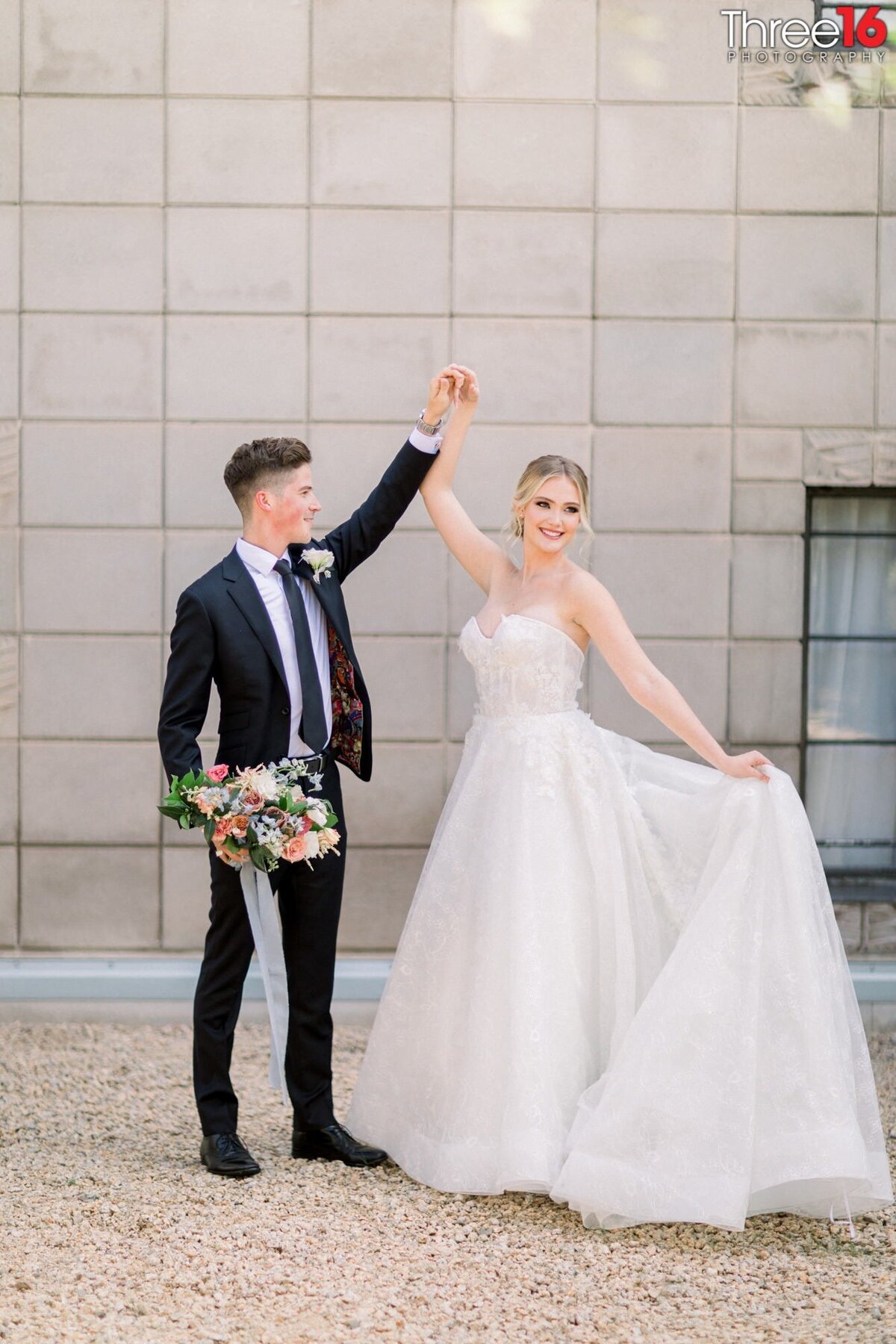 Groom holds his Bride's bouquet as he spins her while she holds up her dress train