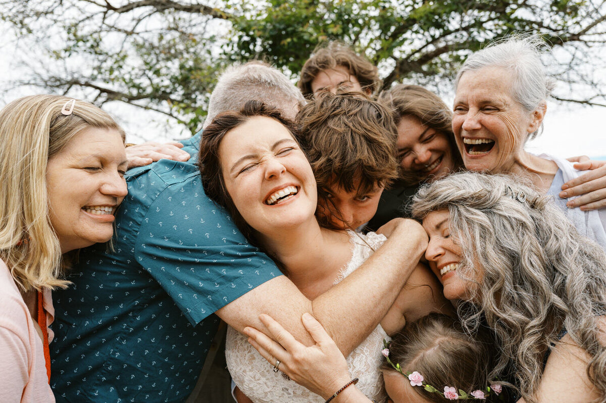Bride is surrounded by wedding guests in a group hug