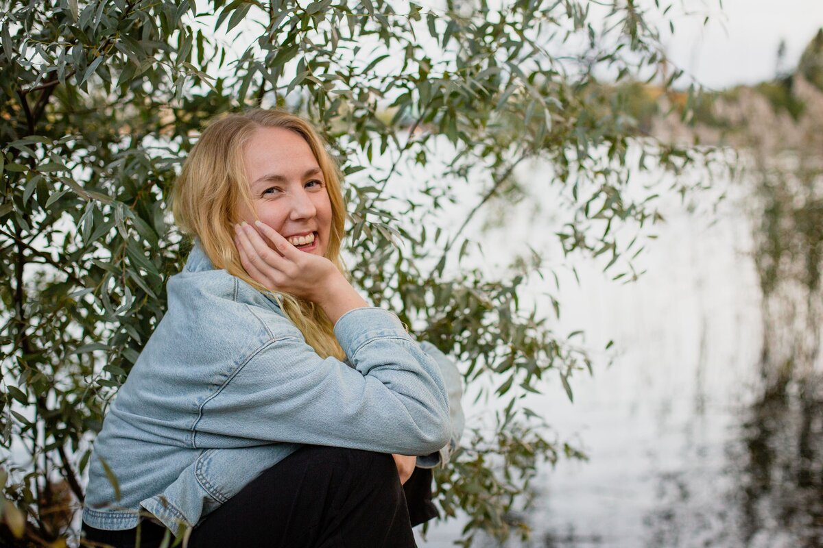 mielen paremminvoinnin ja kehomieliyhteyden valmentaja istuu puun alla ja hymyilee kameralle luonnon keskellä