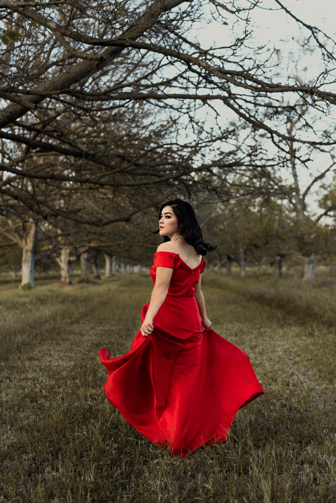 Liz in an epic red dress in the middle of an orchard in Sacramento
