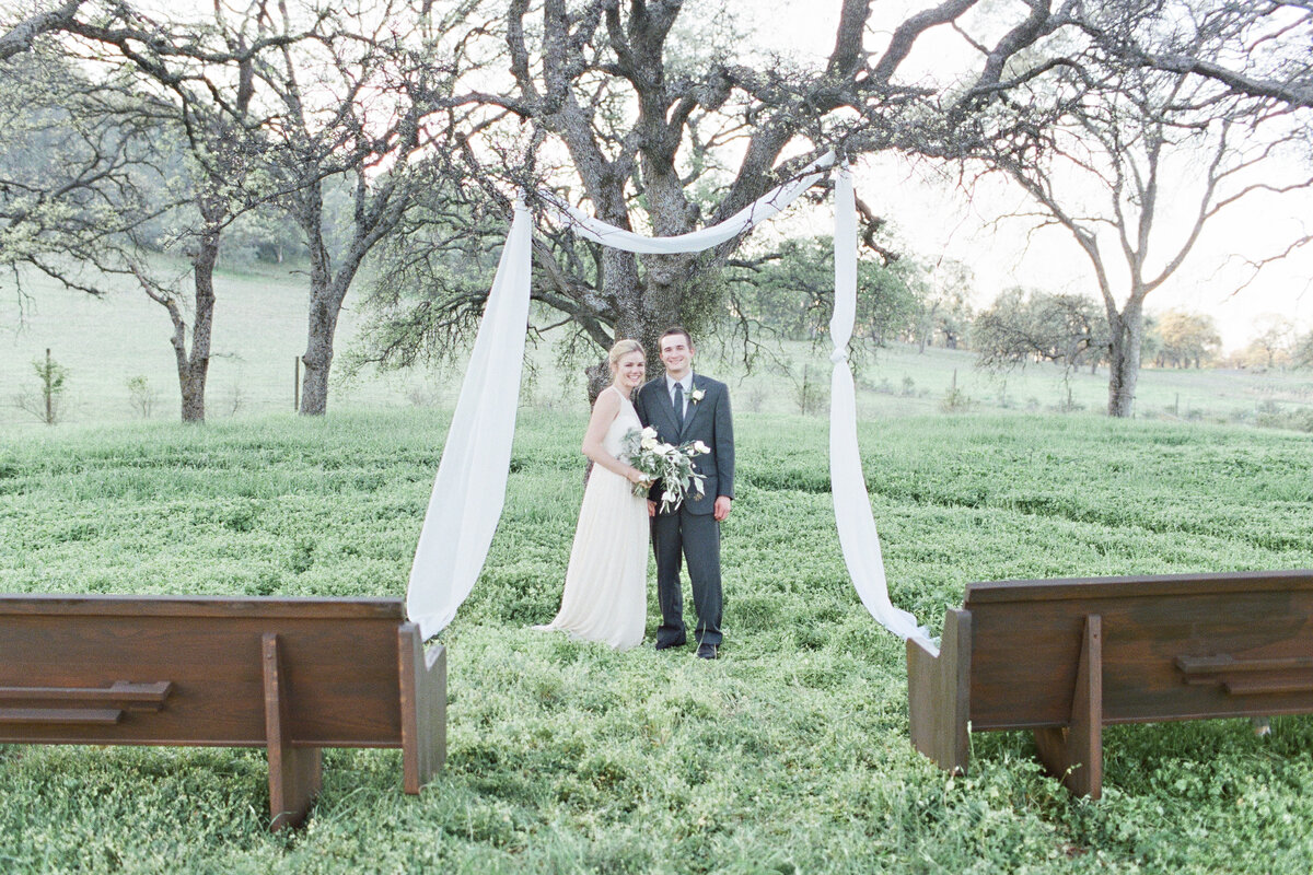 Bride and groom standing at ceremony site under the oak tree at River Highlands Ranch