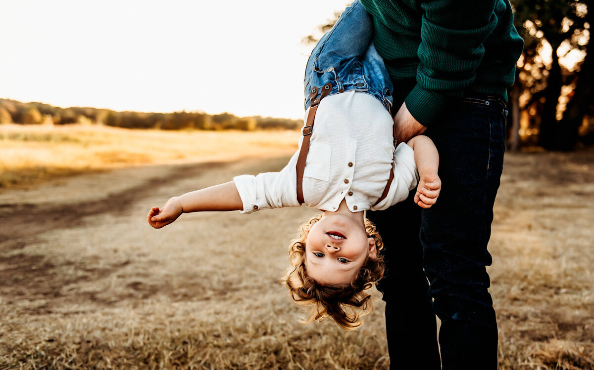 Dad dipping little boy upside down in suspenders.