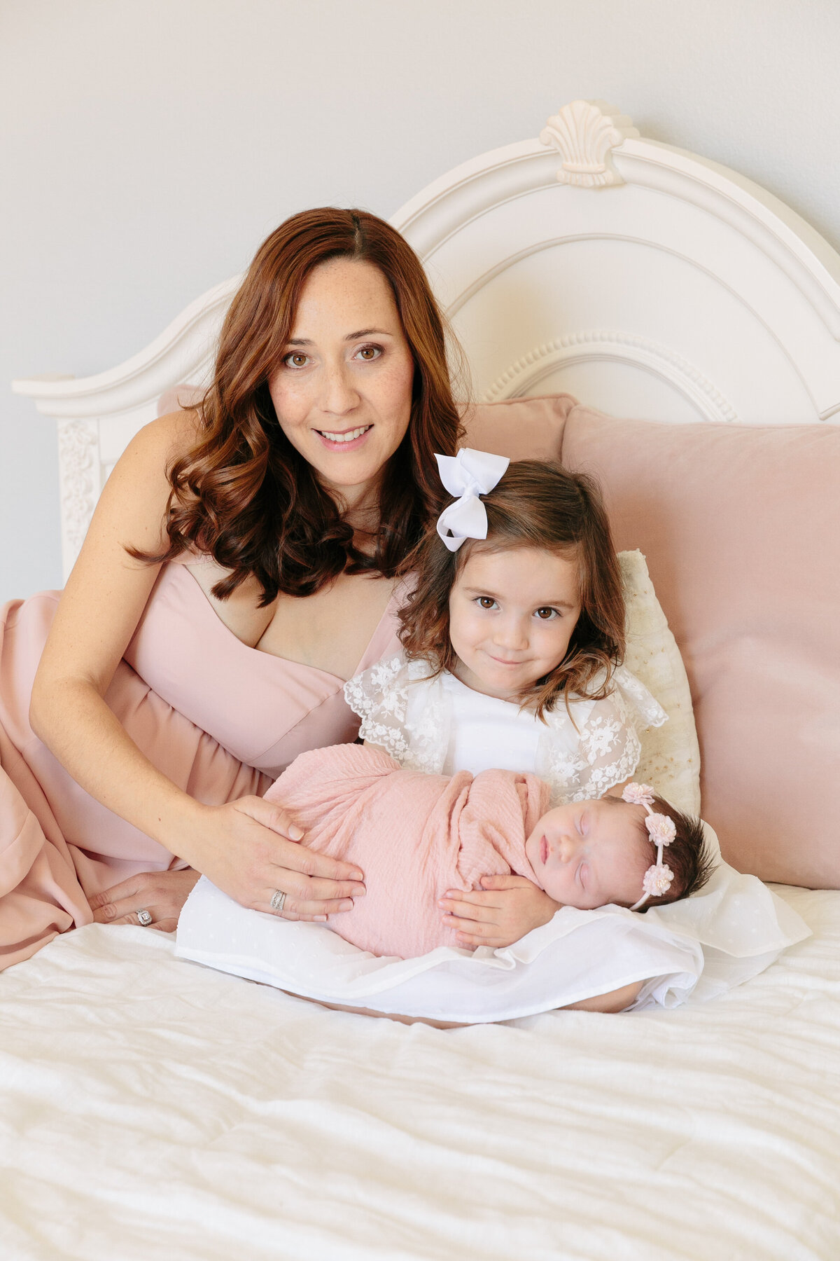 A mom laying on a bed with a small child and a newborn