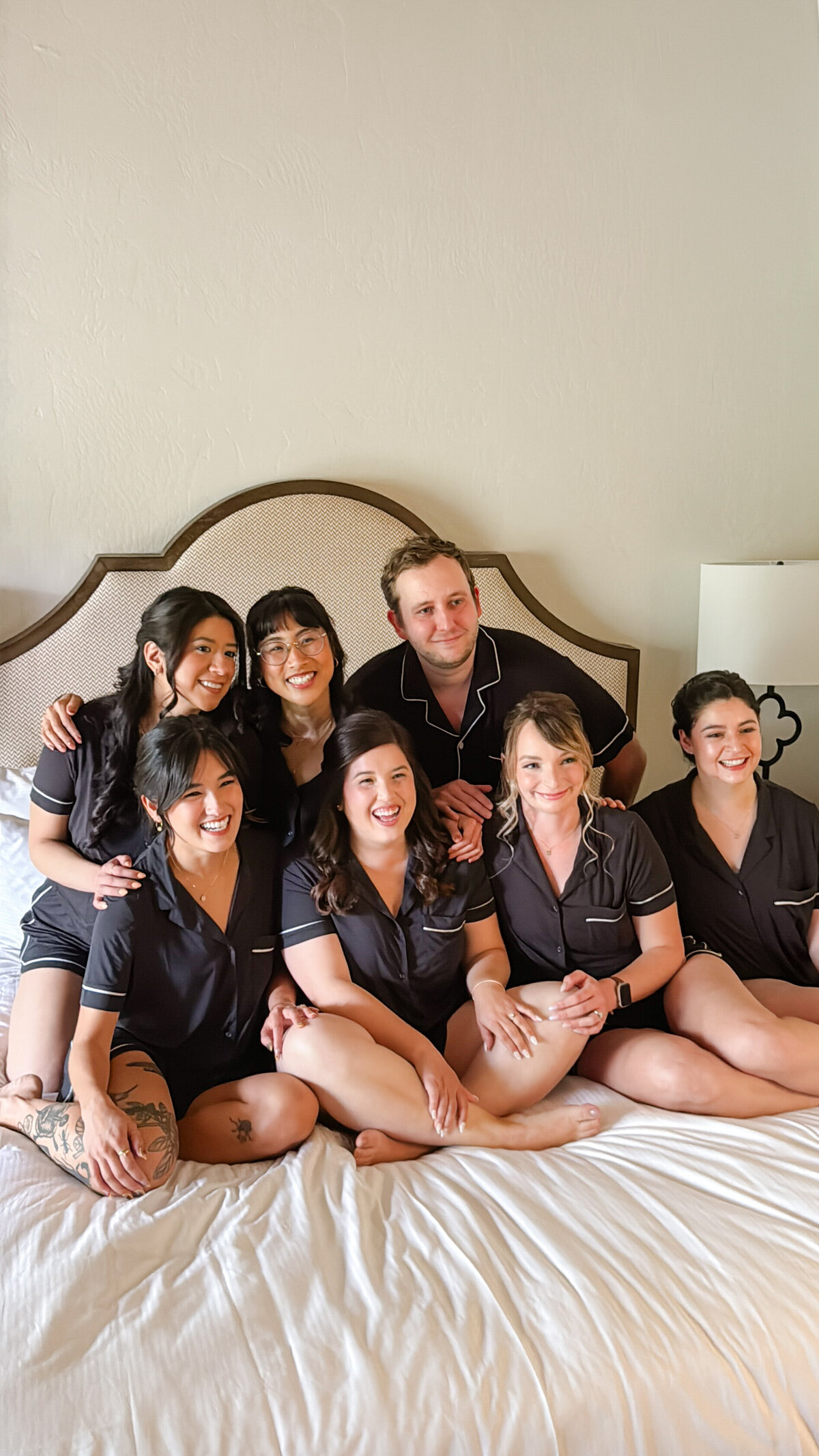 Bride sits smiling with her bridal party in matching black pajama sets on a bed at the Rancho Bernardo Inn.