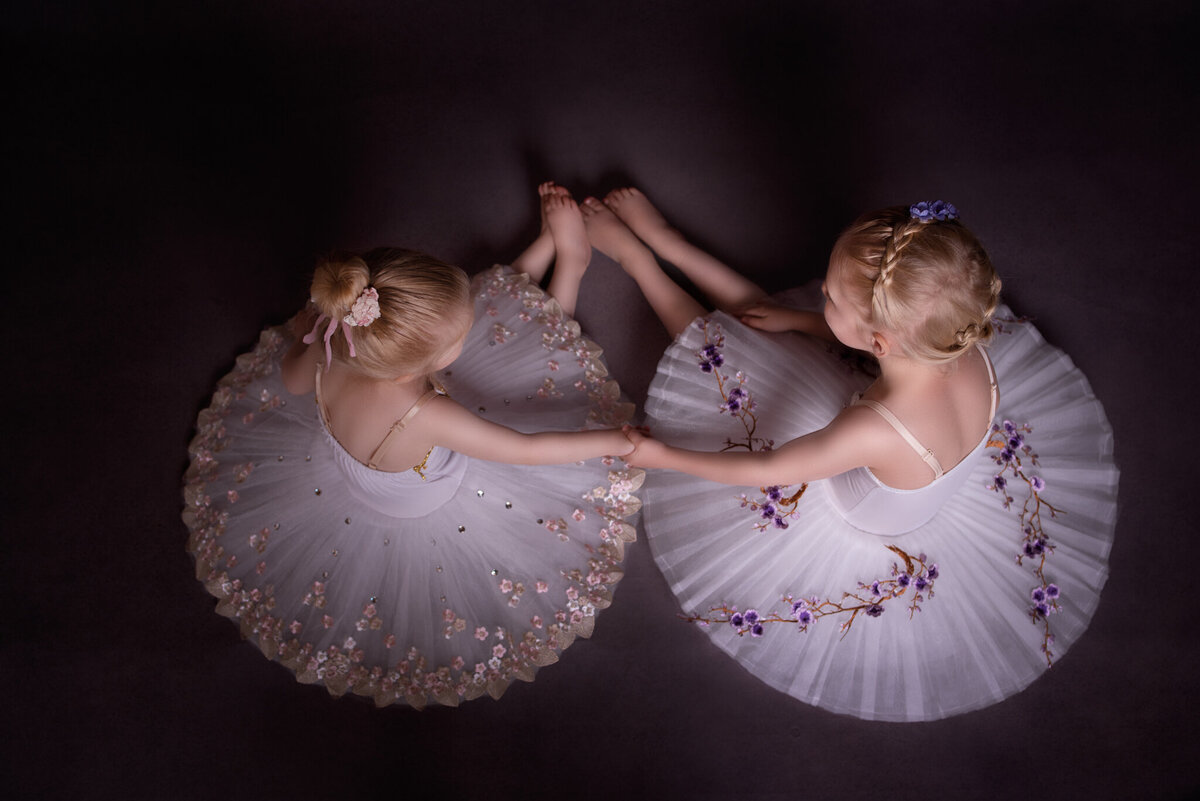 Beautiful fine art portrait of twin ballerinas mirroring each other in delicate white tutus, captured in Overland Park, Kansas. Ideal for families seeking artistic and graceful child photography with a dance theme