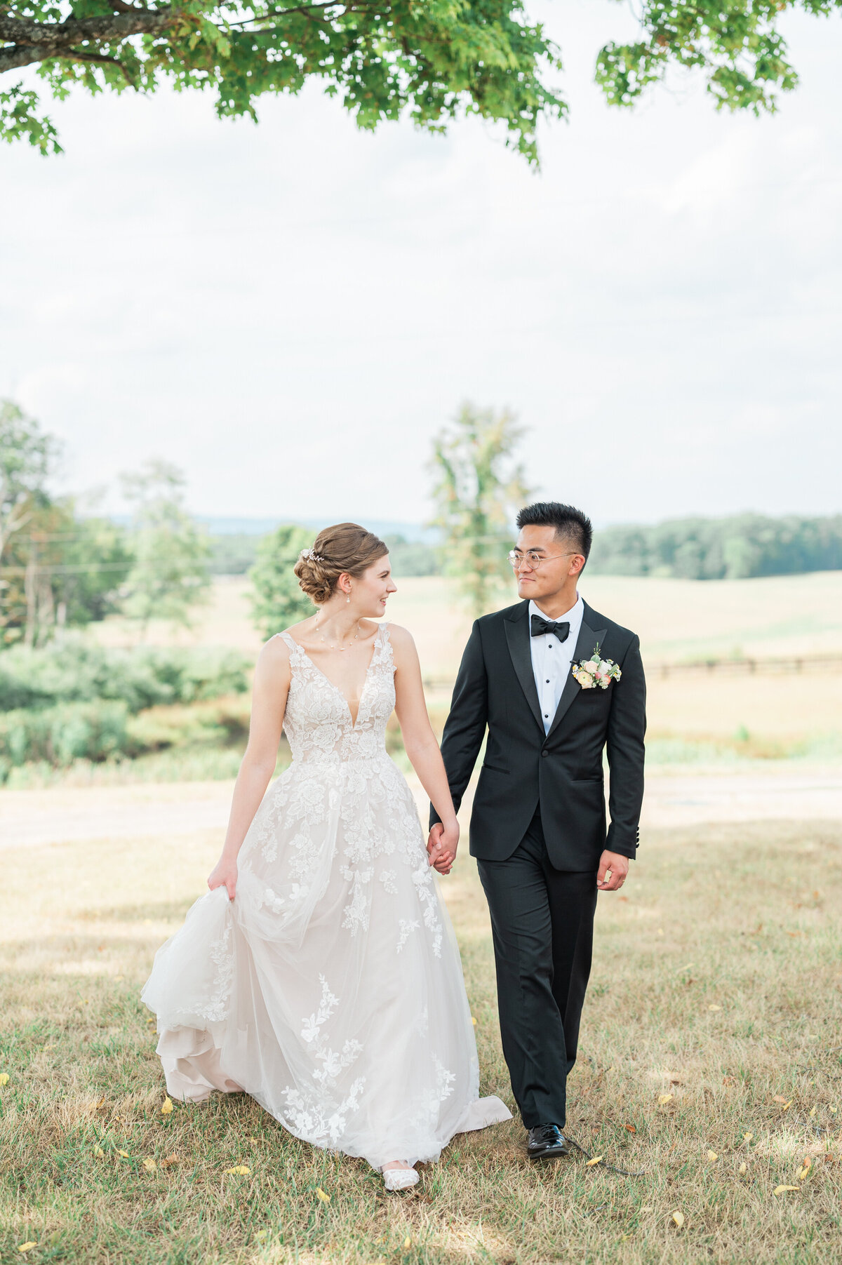 A wedding couple holding hands and smiling at each other as they walk in a field