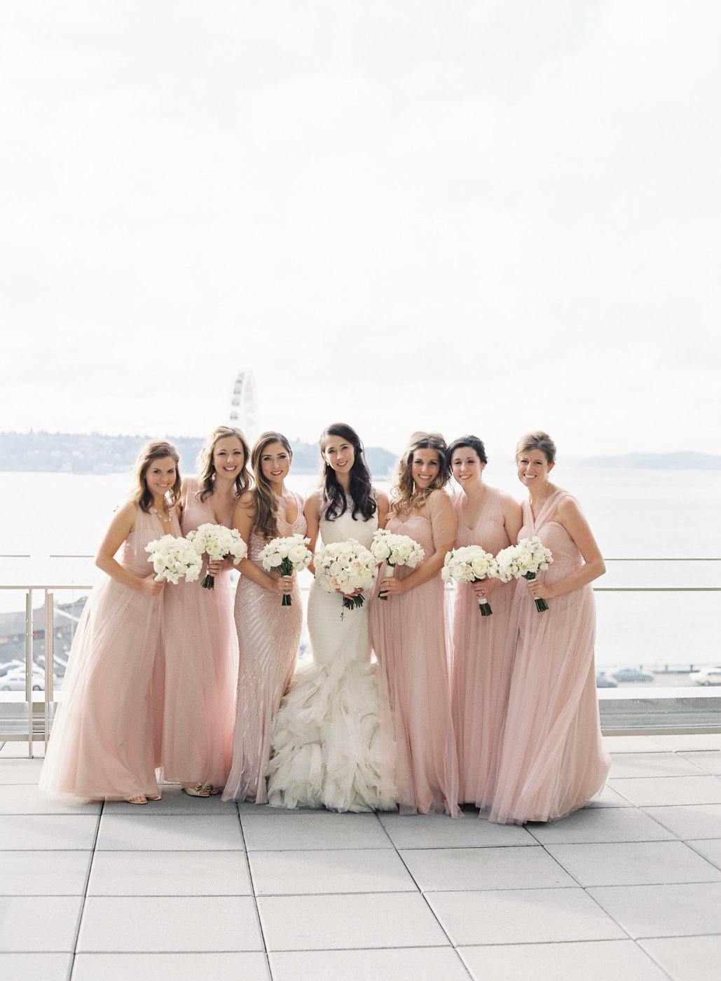 Bridal party in blush dresses with white rose bouquets.