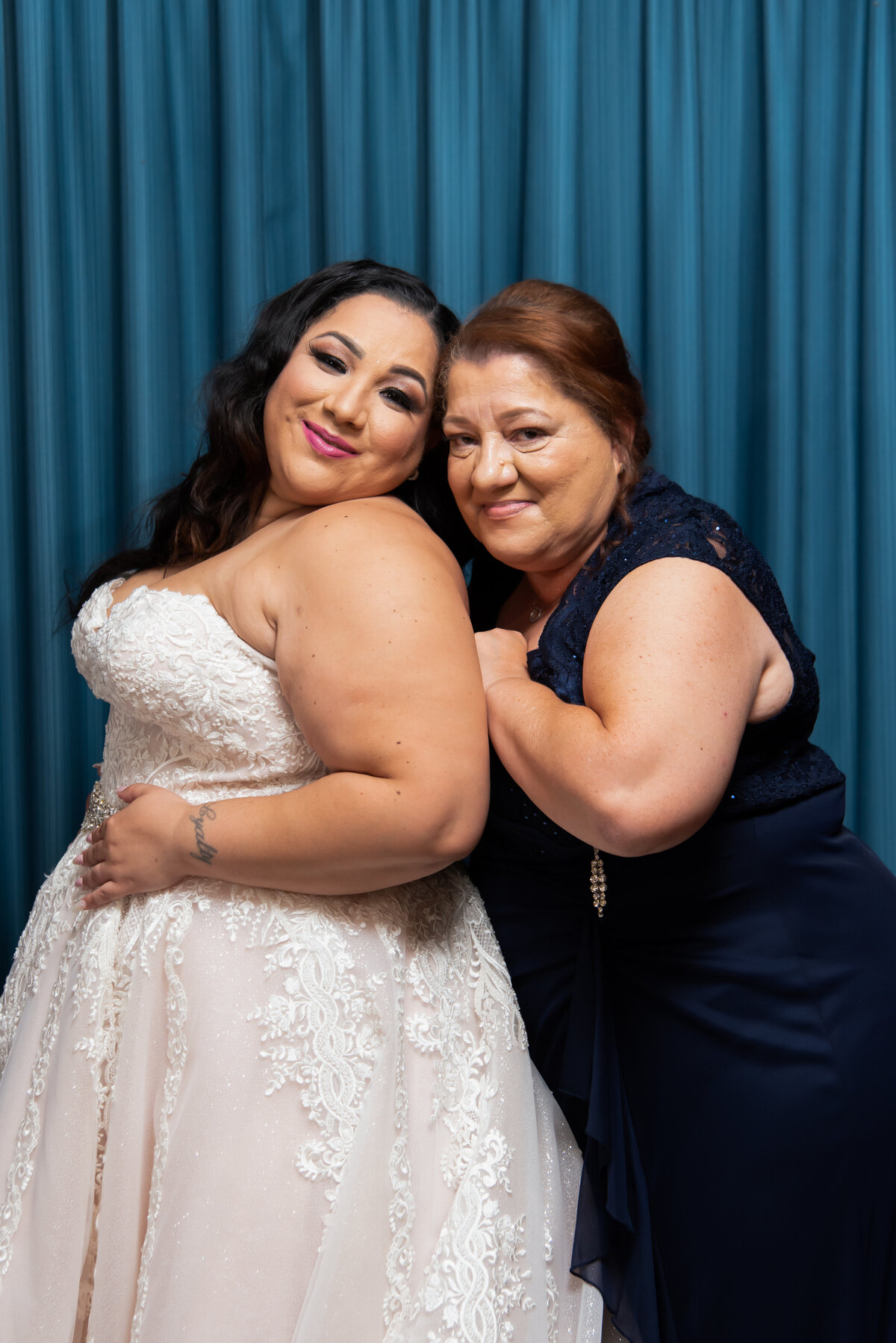 a bride and her mom posed in front of a blue backdrop