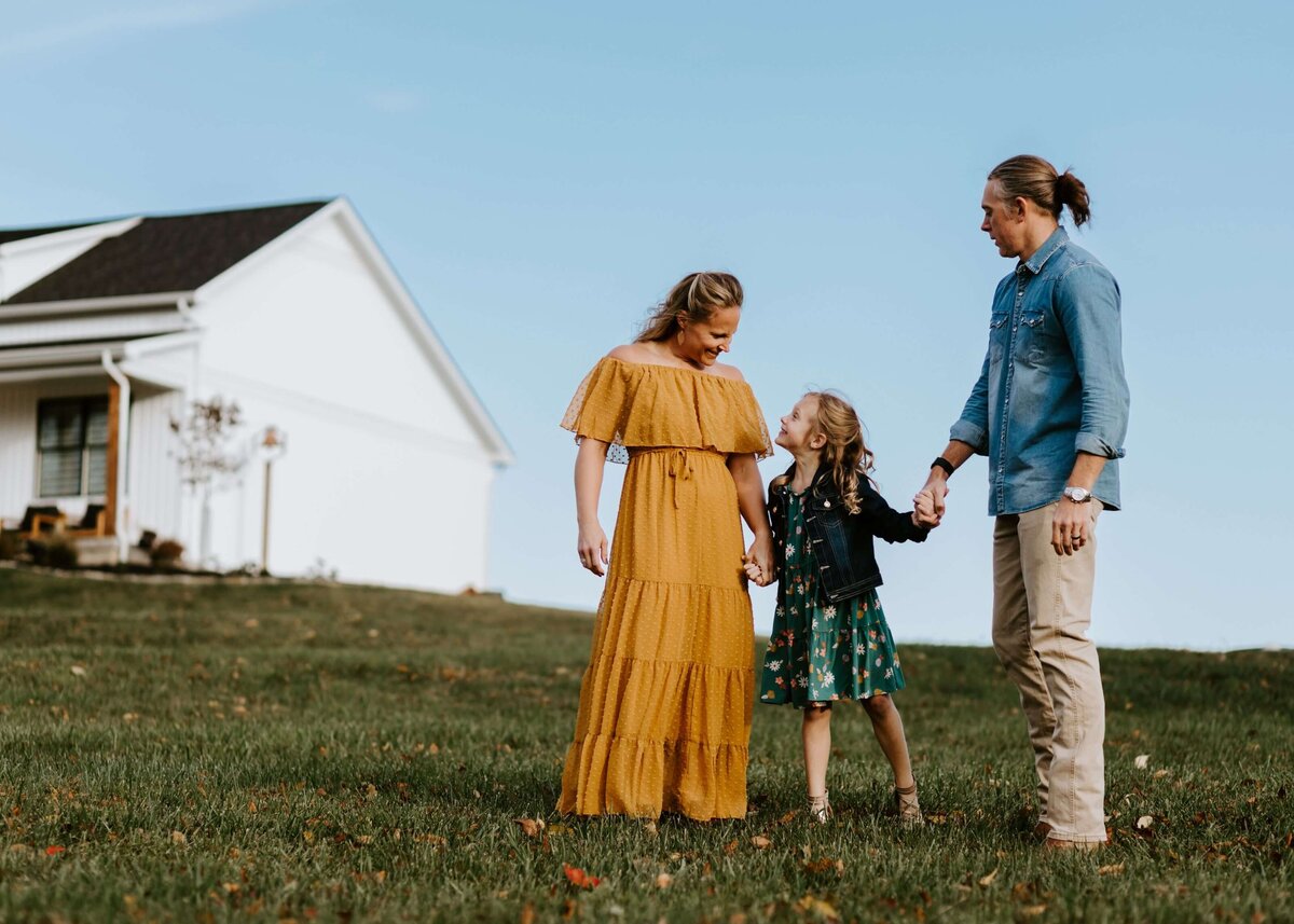 A family holding hands in front of a farmhouse captured by a Pittsburgh family photographer.