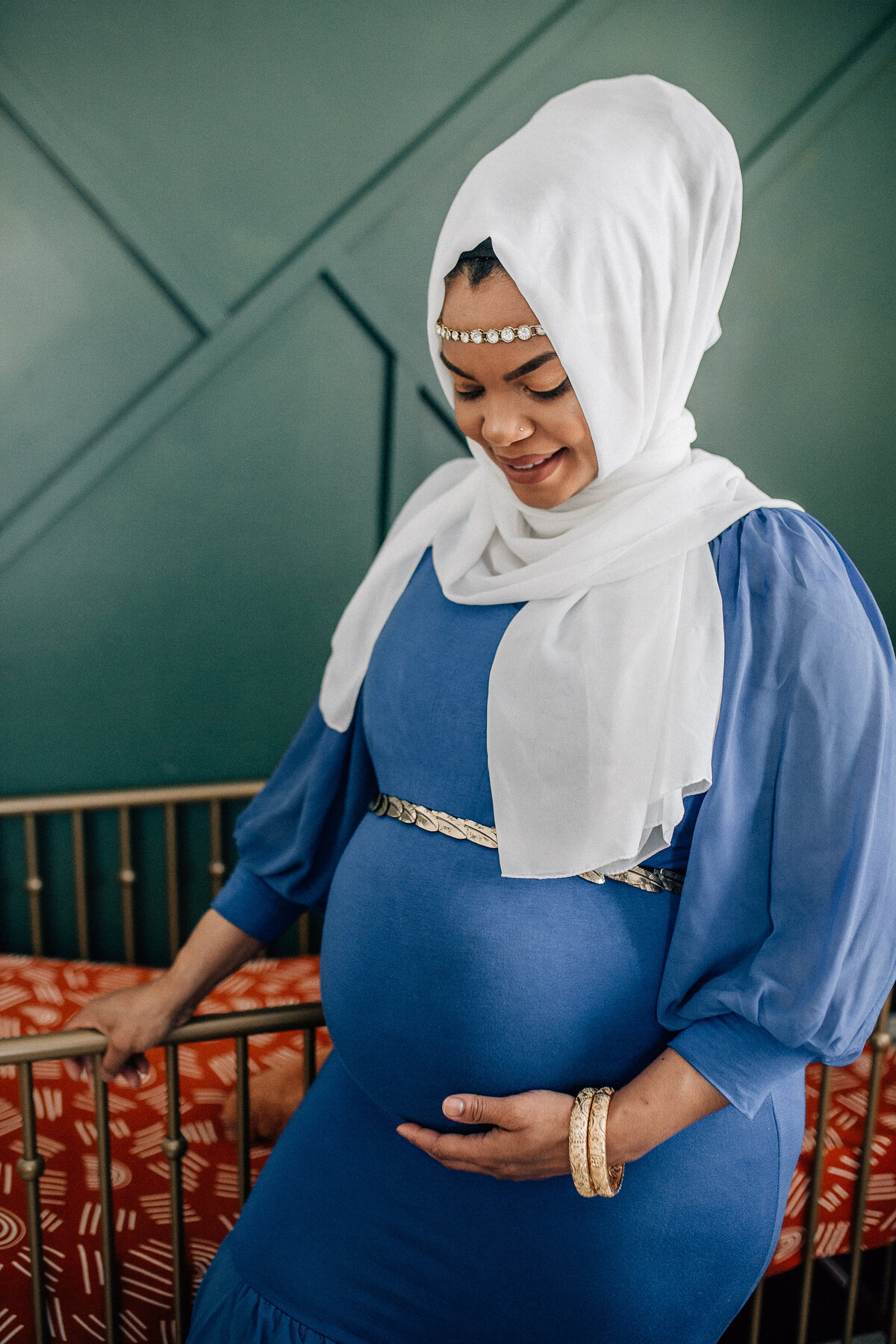 Soon to be mom stands next to a wooden crib and holds her belly.