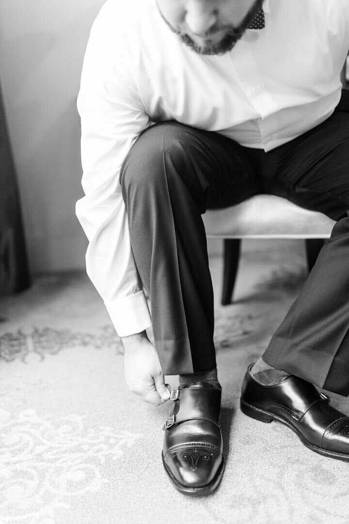 B&W fine art Arkansas photography of groom buckling his shoes.
