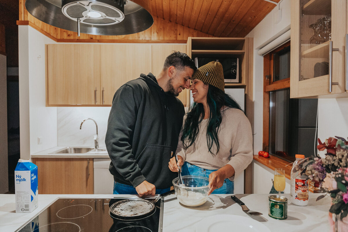 Husband and wife stand forehead to forehead in their cozy Iceland cottage kitchen 