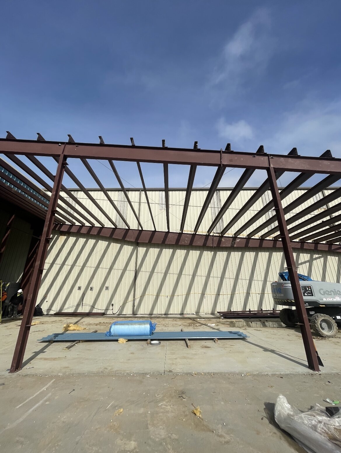 Welded steel columns and beams forming the structural framework for a commercial steel building roof during erection phase.