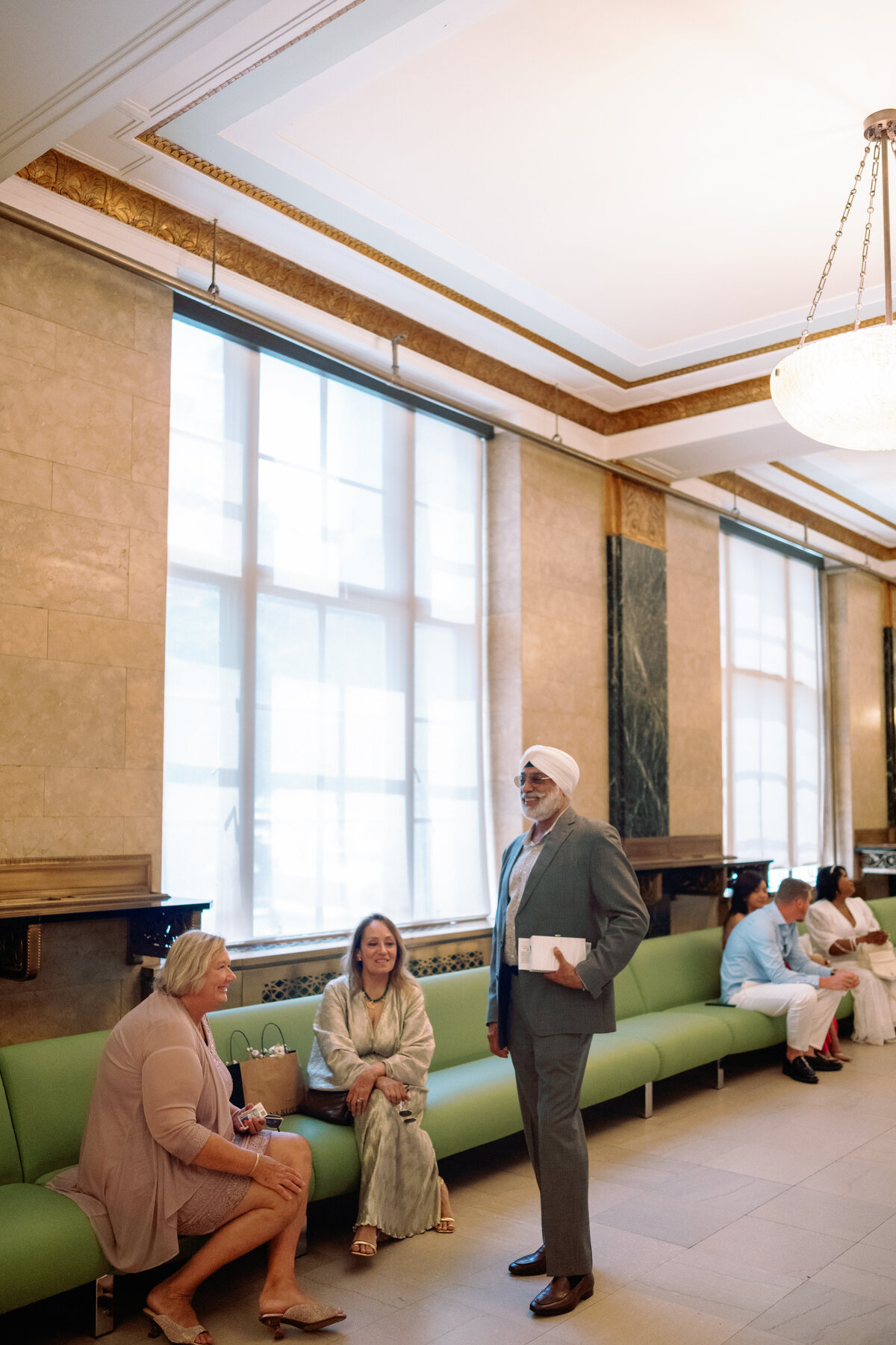 Family members seated on the benches inside New York City Hall while waiting for the wedding ceremony, captured during Japna and Chris’s intimate elopement by NYC wedding photographer Perry Hancock.