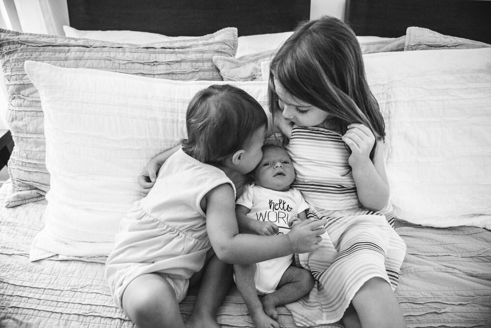 kids kissing baby on bed in Gulf Breeze, florida