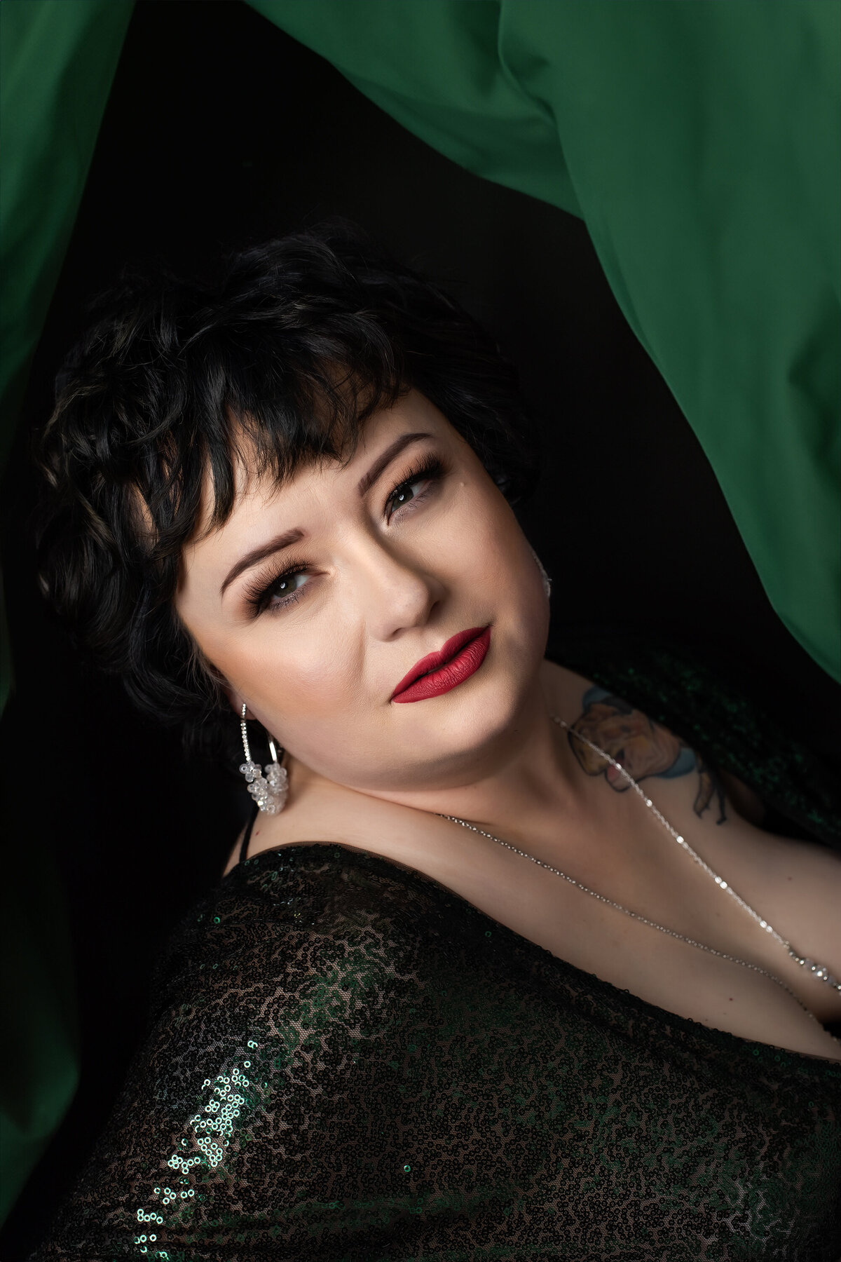 Glamorous portrait on a woman in a green sequin dress with green fabric flowing around her