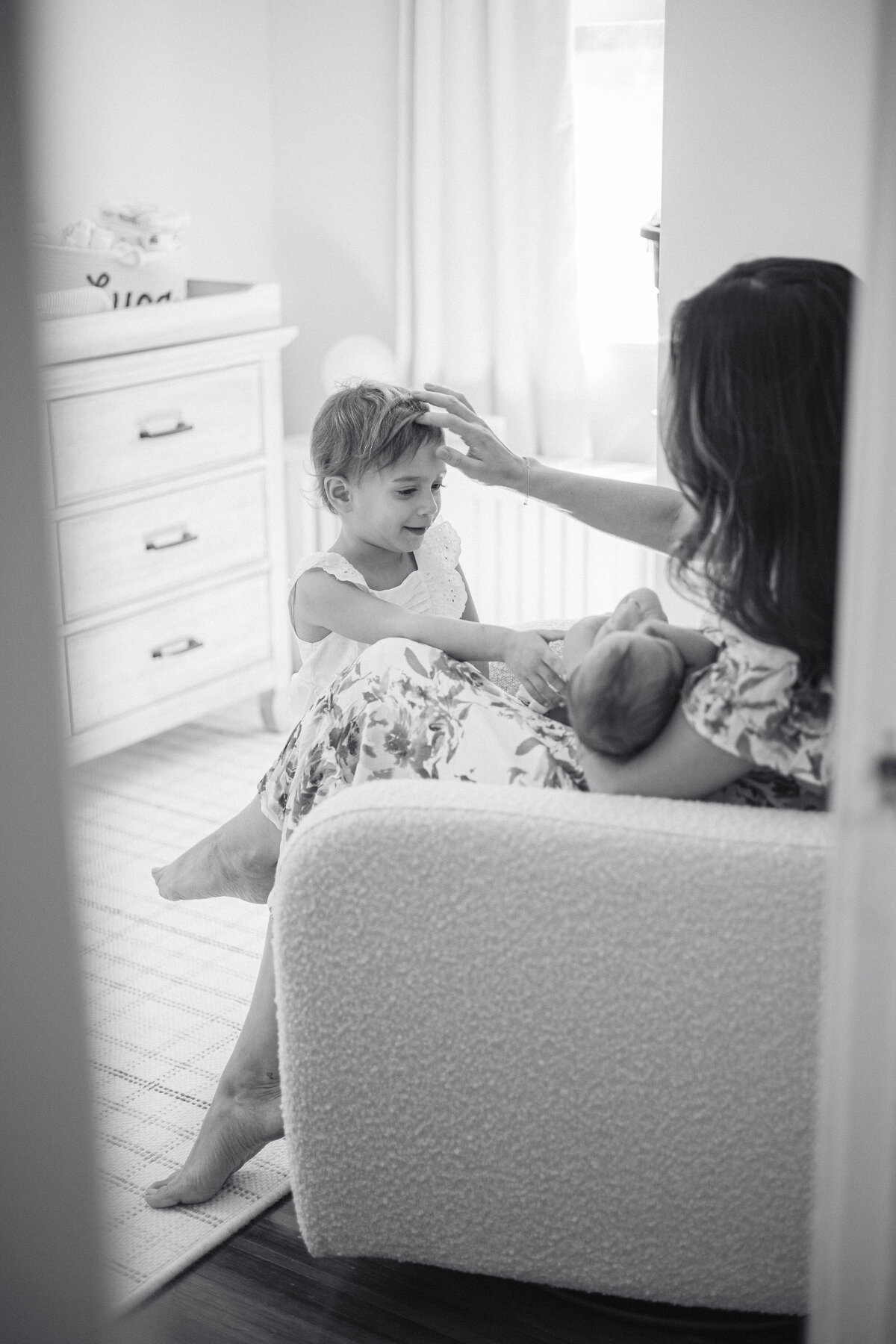 Peeking into the nursery as mom rocks her newborn baby while big sister looks on.