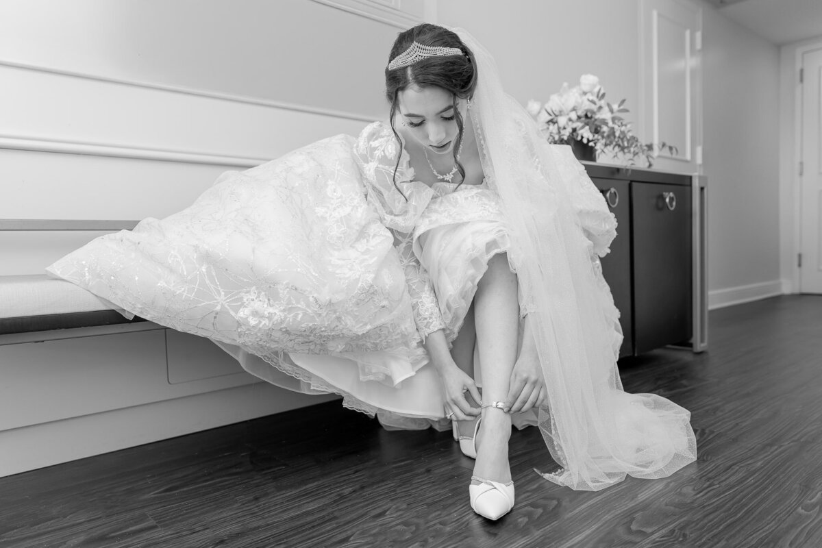 A black and white photo of a bride fixing her shoe before her wedding ceremony.