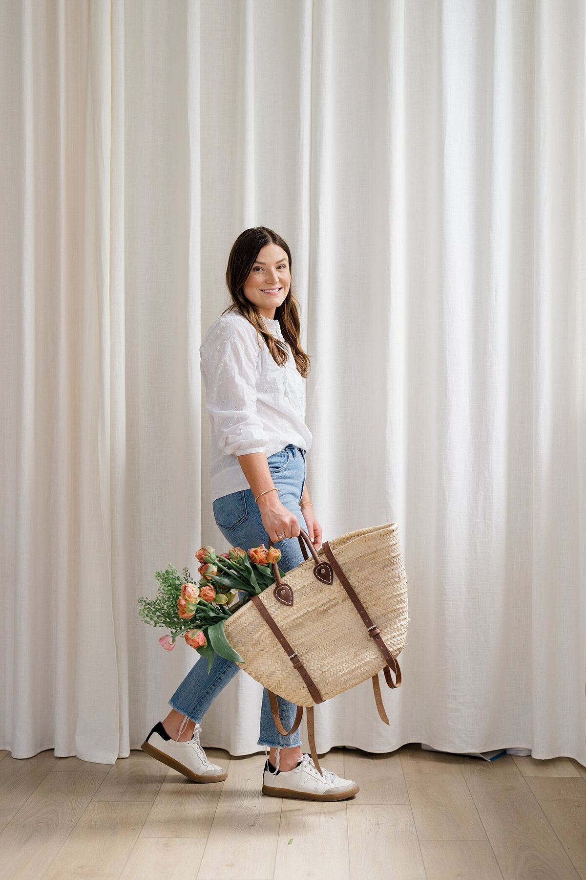 candid branding photos by Columbus photographer with woman carrying a bag with flowers in it with a white curtain backdrop
