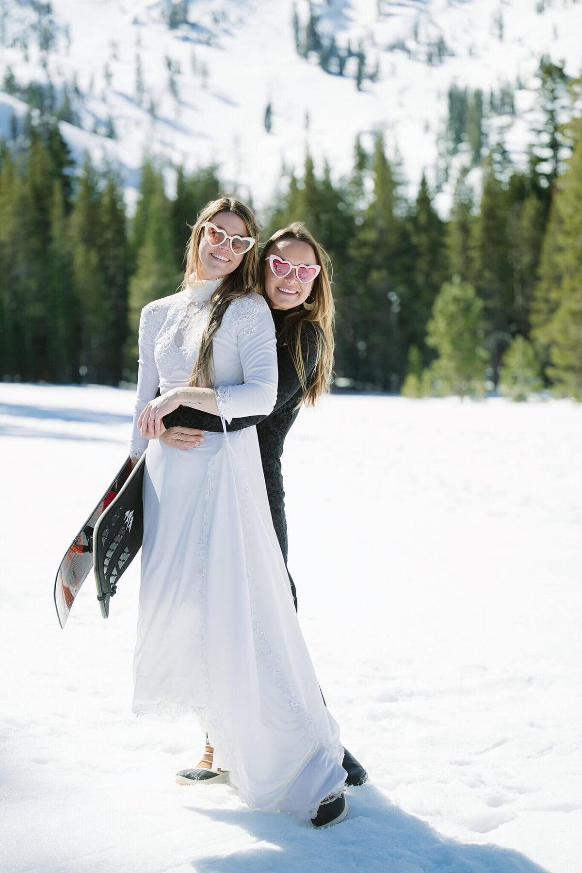 bride and her sister pose for camera while holding snowskate after eloping in Tahoe during winter