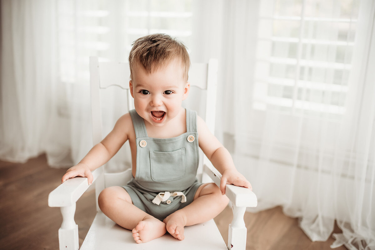 one year old boy sitting in white rocking chair