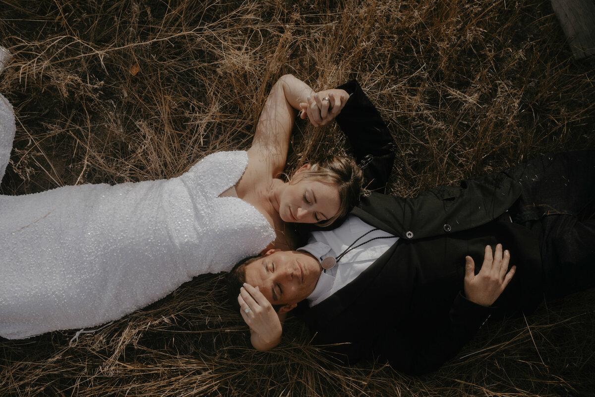 Bride and Groom laying down in meadow during sunset holding hands in reno nevada