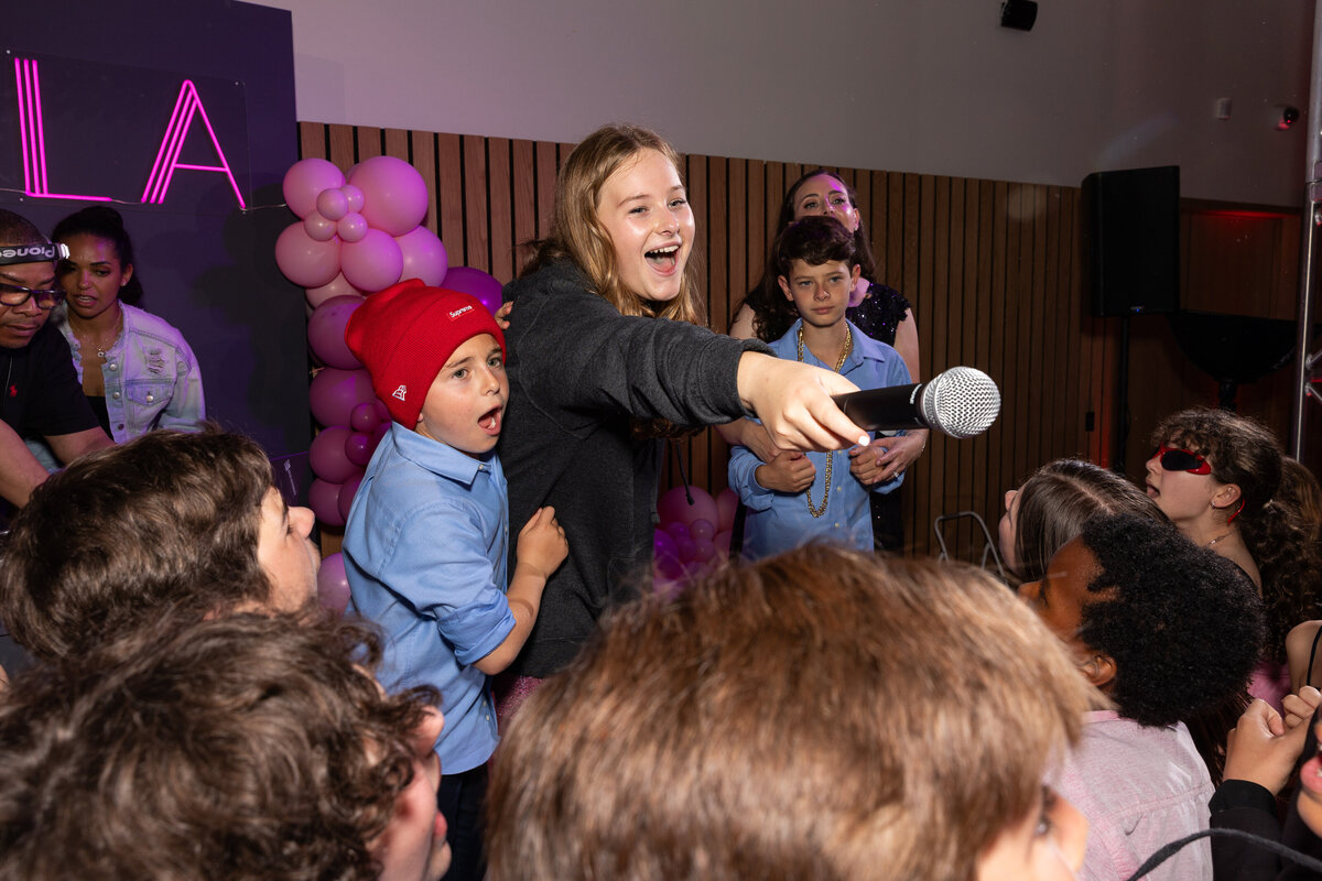 Kids on a stage holding out a mic during a party