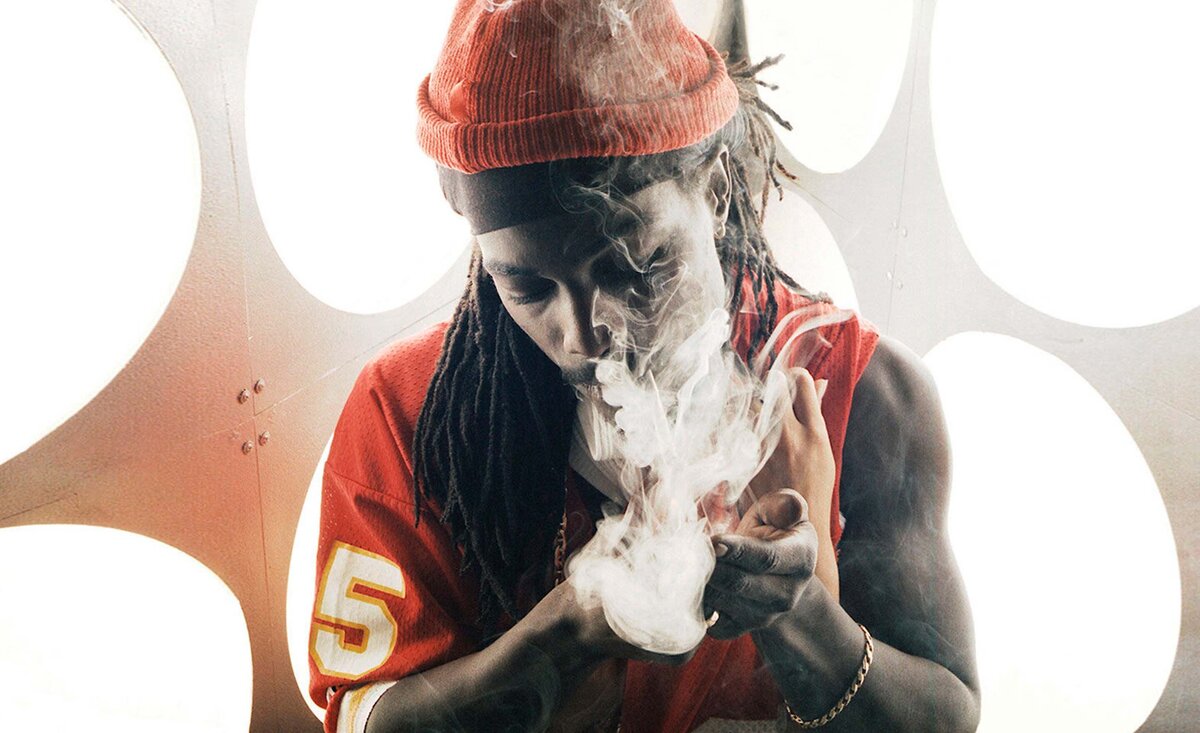 Male musician portrait Red 1 wearing red football jersey puffing smoke with large circle lights behind
