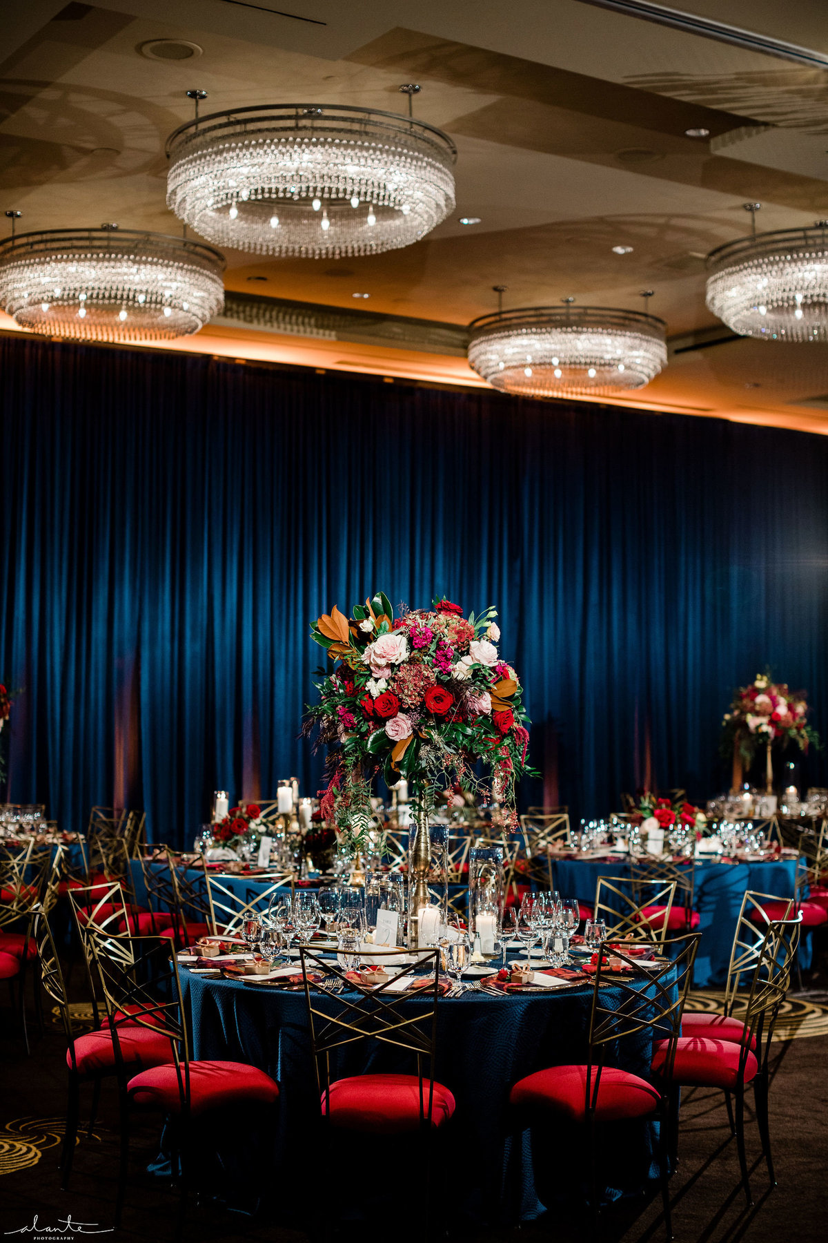 Four Seasons ballroom wedding with navy blue wall draping, blue linens, and Chameleon chairs with  deep red chair cushions