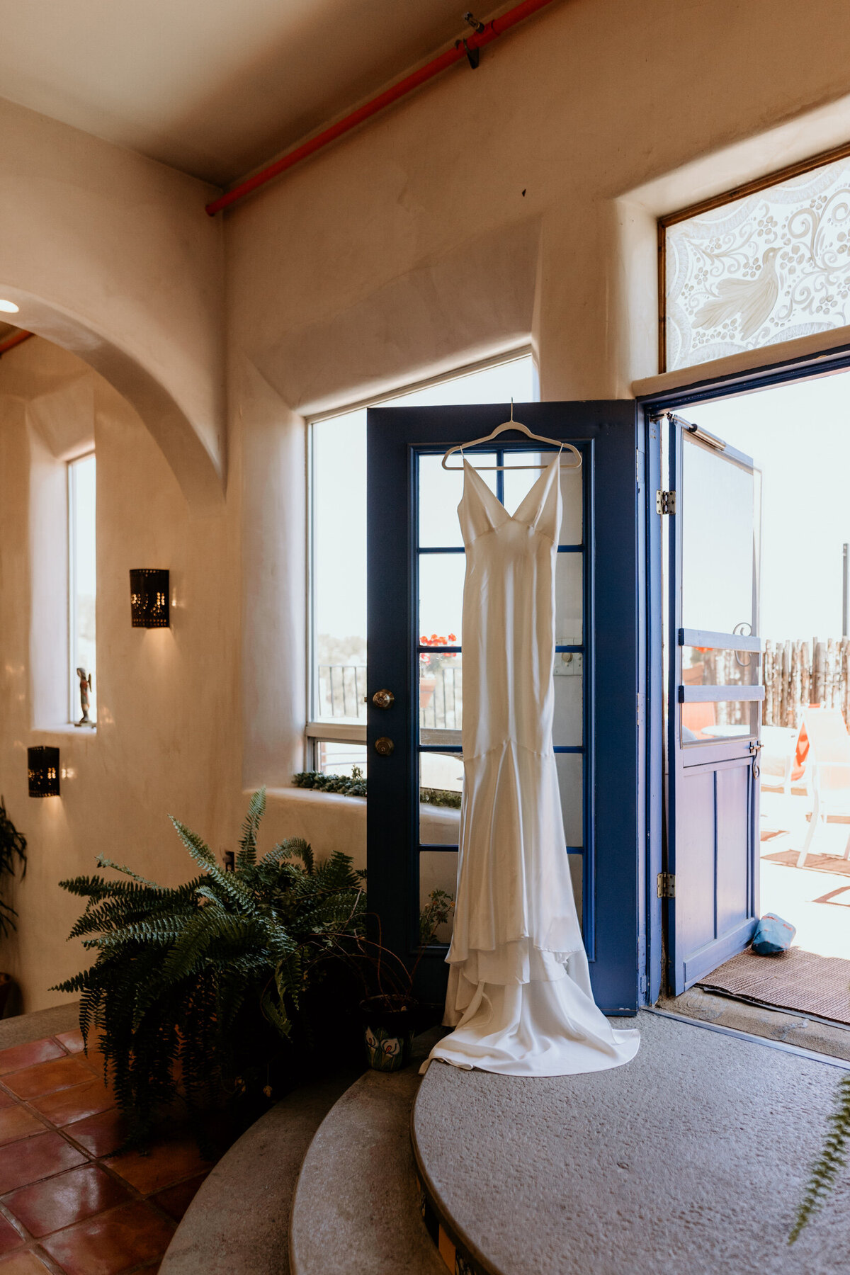 white silk wedding dress hanging on a turquoise door