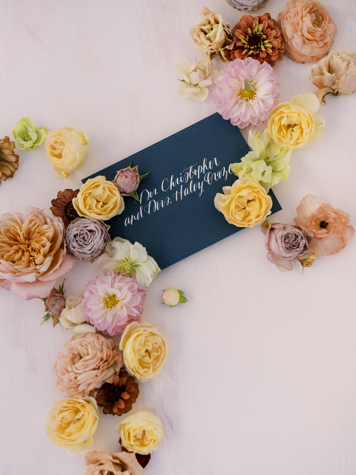 Romantic flatlay with pastel blooms and elegant navy envelope—luxury wedding details with a personal touch.