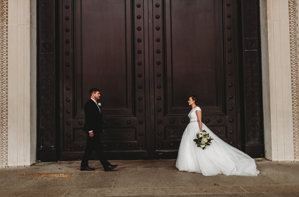 Bride and groom walking towards each other on a large concrete porch of a building in Washington DC as the brides train glides behind her captured by Maryland wedding photographer