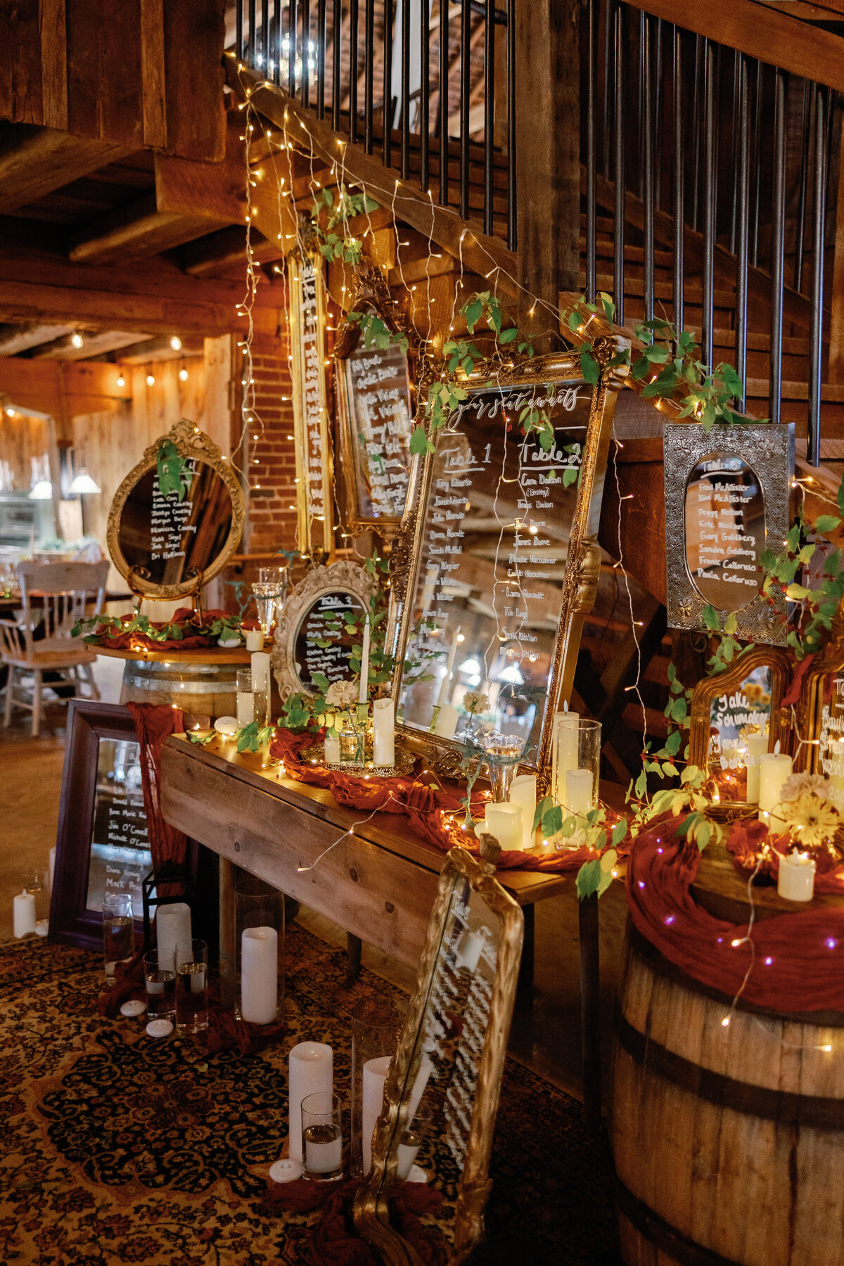 Reception décor at rustic barn with twinkle lights, greenery, and hand-lettered signage on mirrors.