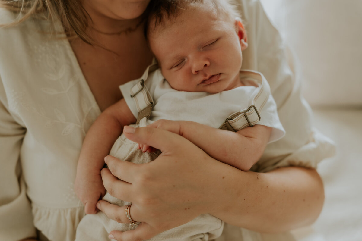 Baby ligt te slapen in de armen van de mama, mama kijkt toe en geniet van het moment. De fotoshoot is aan huis te Asse.