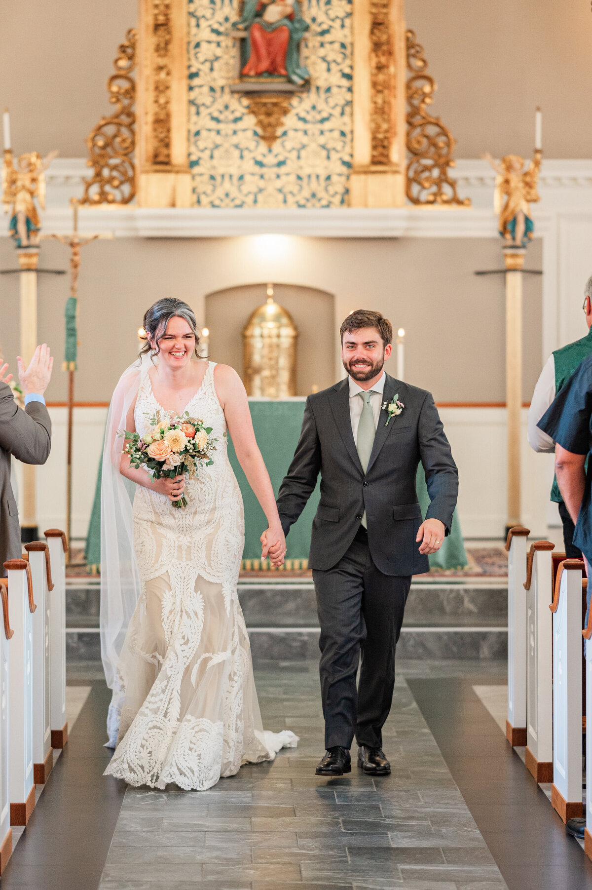 A newlywed couple holding hands and smiling as they walk back up the aisle